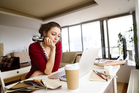 Pensive woman sitting at desk in the living room looking at laptop stock photo