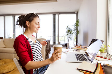 Lächelnde Frau mit Kaffee zum Mitnehmen im Home Office - HAPF01907