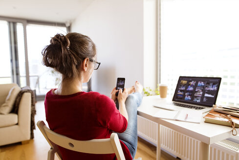 Woman sitting at desk at home using smartphone - HAPF01912