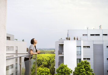 Frau mit Tasse Kaffee auf dem Balkon stehend - HAPF01915