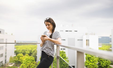 Frau benutzt Smartphone auf Balkon, lizenzfreies Stockfoto