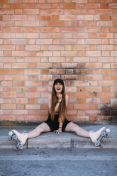 Portrait of laughing young woman with roller skates sitting on sidewalk - JPF00252