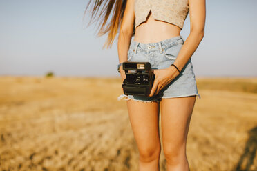 Young woman with instant camera on a field at sunset, partial view - JPF00253