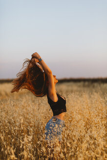Junge Frau steht in einem Getreidefeld und genießt den Sonnenuntergang - JPF00254
