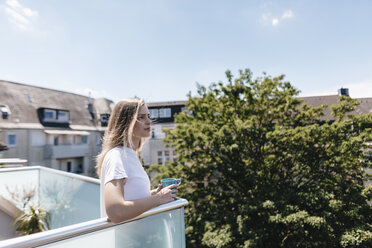 Junge Frau auf einem Balkon, Tee trinkend - GUSF00095