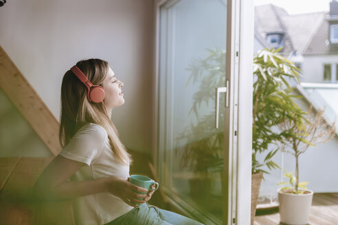 Junge Frau entspannt sich zu Hause mit einer Tasse Tee und hört Musik - GUSF00096