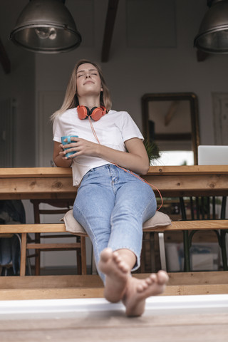 Junge Frau entspannt sich zu Hause mit einer Tasse Tee und hört Musik, lizenzfreies Stockfoto