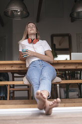 Young woman relaxing at home with a cup of tea, listening music - GUSF00098