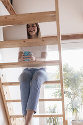 Junge Frau sitzt auf einer Holztreppe und benutzt einen Laptop - GUSF00106