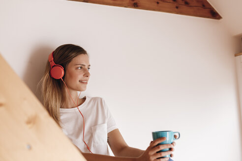 Junge Frau entspannt sich zu Hause mit einer Tasse Tee und hört Musik - GUSF00108