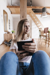 Young woman sitting at home using digital tablet - GUSF00109