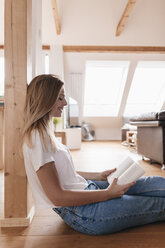 Junge Frau sitzt auf dem Boden und liest ein Buch - GUSF00111