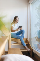 Junge Frau sitzt zu Hause und benutzt ein digitales Tablet - GUSF00114