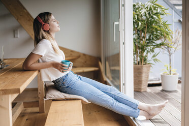 Junge Frau entspannt sich zu Hause mit einer Tasse Tee und hört Musik - GUSF00128