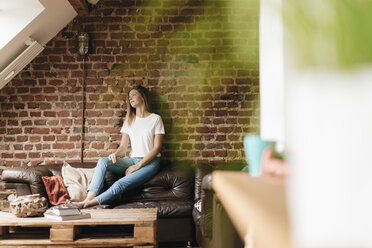 Young woman sitting on couch, daydreaming - GUSF00129