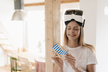 Junge Frau mit VR-Brille, die ihren Urlaub plant und einen Spielzeugstuhl hält - GUSF00165