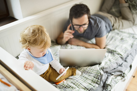 Vater zu Hause mit seinem kleinen Sohn, der Laptop und Mobiltelefon benutzt, lizenzfreies Stockfoto