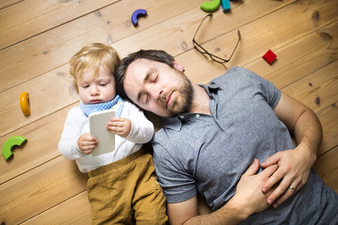 Father lying on floor with his little son playing with smartphone - HAPF01970