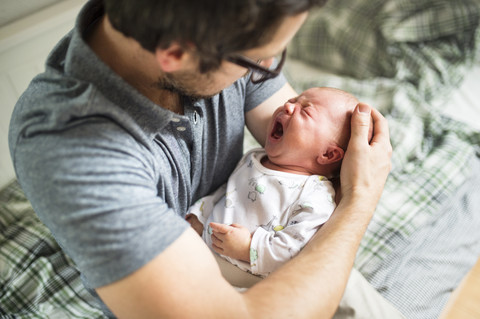 Father at home consoling his crying baby daughter stock photo