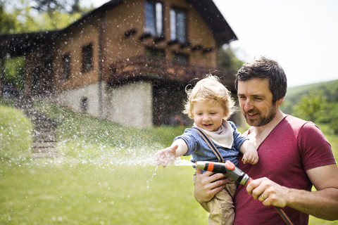 Kleiner Junge bewässert mit seinem Vater den Rasen, lizenzfreies Stockfoto