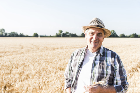 Porträt eines lachenden älteren Landwirts, der vor einem Feld steht, lizenzfreies Stockfoto