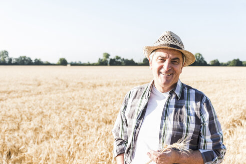 Porträt eines lachenden älteren Landwirts, der vor einem Feld steht - UUF11175