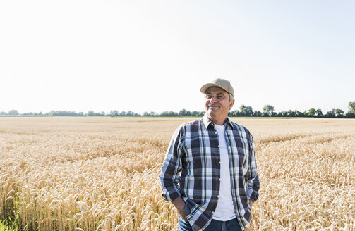 Entspannter älterer Landwirt vor einem Weizenfeld stehend - UUF11182