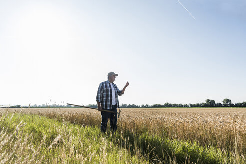 Ein älterer Landwirt steht vor einem Feld und untersucht die Ähren - UUF11184