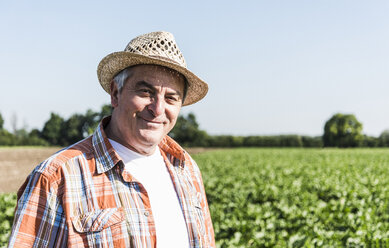 Portrait of content senior farmer standing in front of a field - UUF11204