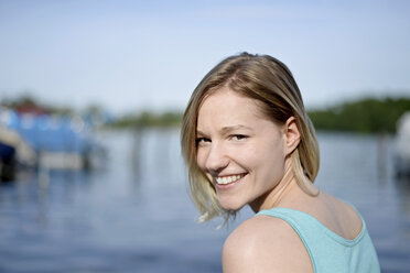 Porträt einer lächelnden jungen Frau vor einem See - BFRF01806