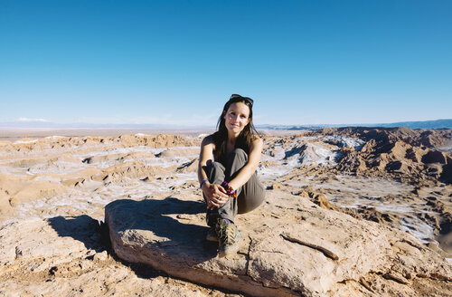 Chile, Atacama-Wüste, lächelnde Frau auf einem Felsen sitzend im Sonnenlicht - GEMF01747