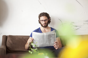 Porträt eines jungen Mannes, der auf einer Couch in einem Café Zeitung liest - MFRF00890