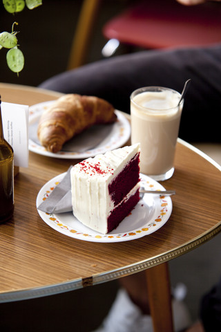 Kuchen, Croissant und ein Glas Latte Macchiato auf einem Tisch, lizenzfreies Stockfoto