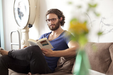 Portrait of smiling young man reading book in a coffee shop - MFRF00896