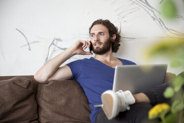 Porträt eines jungen Mannes, der auf einer Couch in einem Café sitzt und telefoniert - MFRF00904