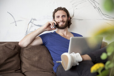 Porträt eines jungen Mannes, der auf einer Couch in einem Café sitzt und telefoniert - MFRF00905