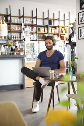 Porträt eines jungen Mannes, der in einem Café sitzt und einen Laptop benutzt - MFRF00909