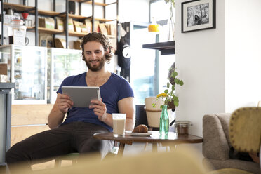 Portrait of young man sitting in a coffee shop using tablet - MFRF00911