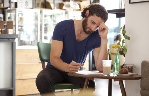 Nachdenklicher junger Mann sitzt in einem Café und schreibt einen Brief - MFRF00913