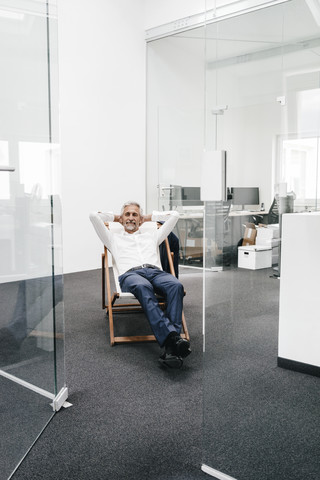 Smiling mature businessman relaxing on deck chair in office stock photo