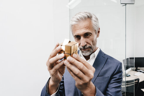 Mature businessman in office examining Rubik's Cube - KNSF02111