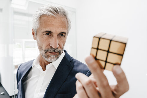 Reifer Geschäftsmann im Büro, der den Rubik's Cube untersucht - KNSF02113