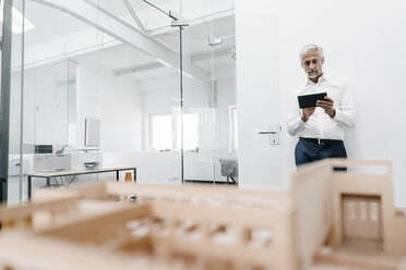 Älterer Geschäftsmann mit Architekturmodell und Tablet im Büro - KNSF02114