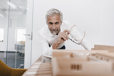 Mature businessman examining architectural model in office - KNSF02118