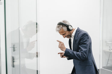 Happy mature businessman in office wearing headphones - KNSF02121