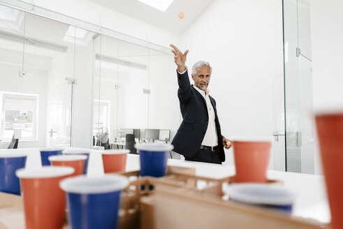 Mature businessman with architectural model in office throwing a ball - KNSF02129