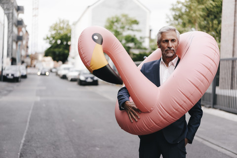 Mature businessman on the street with inflatable flamingo stock photo