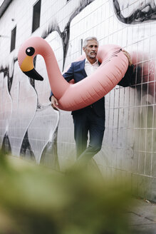 Mature businessman outdoors with inflatable flamingo - KNSF02137