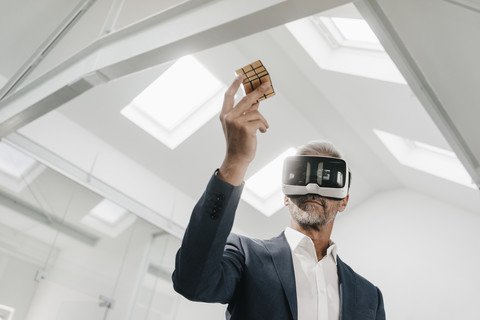 Mature businessman in office wearing VR glasses holding Rubik's Cube stock photo