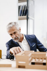 Älterer Geschäftsmann, der ein architektonisches Modell im Büro untersucht - KNSF02147